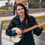 Annie Bartholomew plays a song from her upcoming debut album Sisters of White Chapel on a clawhammer banjo on a bench at Mayor Bill Overstreet Park on Thursday. The longtime local folk musician said she learned the instrument specifically for the project, and both the character of the instrument and women who played it during the Klondike Gold Rush helped inspire the mostly original songs she performs on the album. (Mark Sabbatini / Juneau Empire)