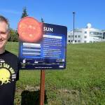 Peter Delamere pauses in front of a UAF Planet Walk sign at the University of Alaska Fairbanks, with the International Arctic Research Center and the Geophysical Institute in the background. (Photo by Ned Rozell)