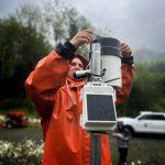 A Prince of Wales Alaska Youth Stewards crew member adjusts tipping bucket and rain gauge on Port Saint Nicholas Road. This device measures rainfall. (Photo by Zofia Danielson)