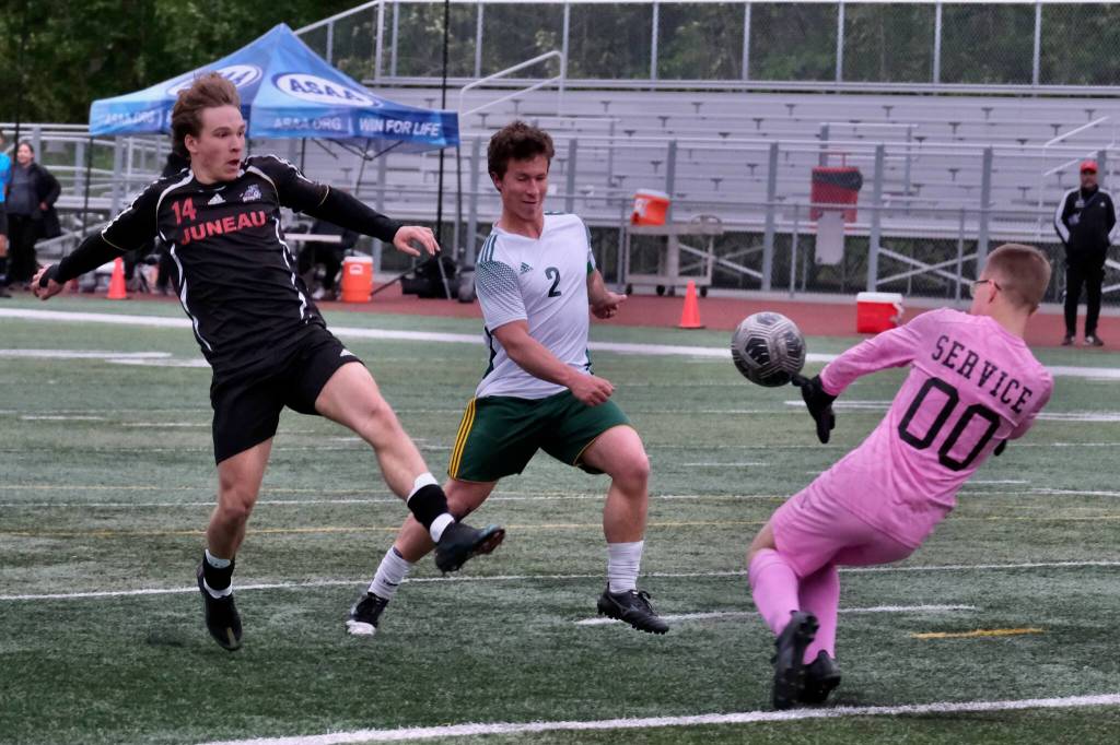 Juneau-Douglas High School: Yadaa.at Kalé senior Kai Ciambor touches a shot past Service sophomore keeper Nathaniel Thate and senior Matej Omalley (2) during the Crimson Bears win over Service to open the 2025 ASAA/First National Bank Alaska Soccer State Championships at Wasilla High School on Thursday, May 29, 2025. (Klas Stolpe / Juneau Empire)