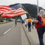 Participants in No Kings protest walk down Egan Drive waving an American flag on Saturday, June 14, 2025 (Natalie Buttner / Juneau Empire)
