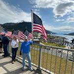 People supporting the U.S. Army on its 250th anniversary gather on the Douglas Bridge on Saturday, June 14, 2025, while a No Kings protest takes place in the backdrop. (Mark Sabbatini / Juneau Empire)