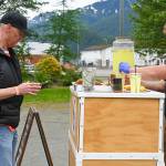 Andy Engstrom (left) uses bitcoin to buy lemonade and cookies from business owner Denali Schijvens (right) on Saturday, July 5, 2025. (Jasz Garrett / Juneau Empire)