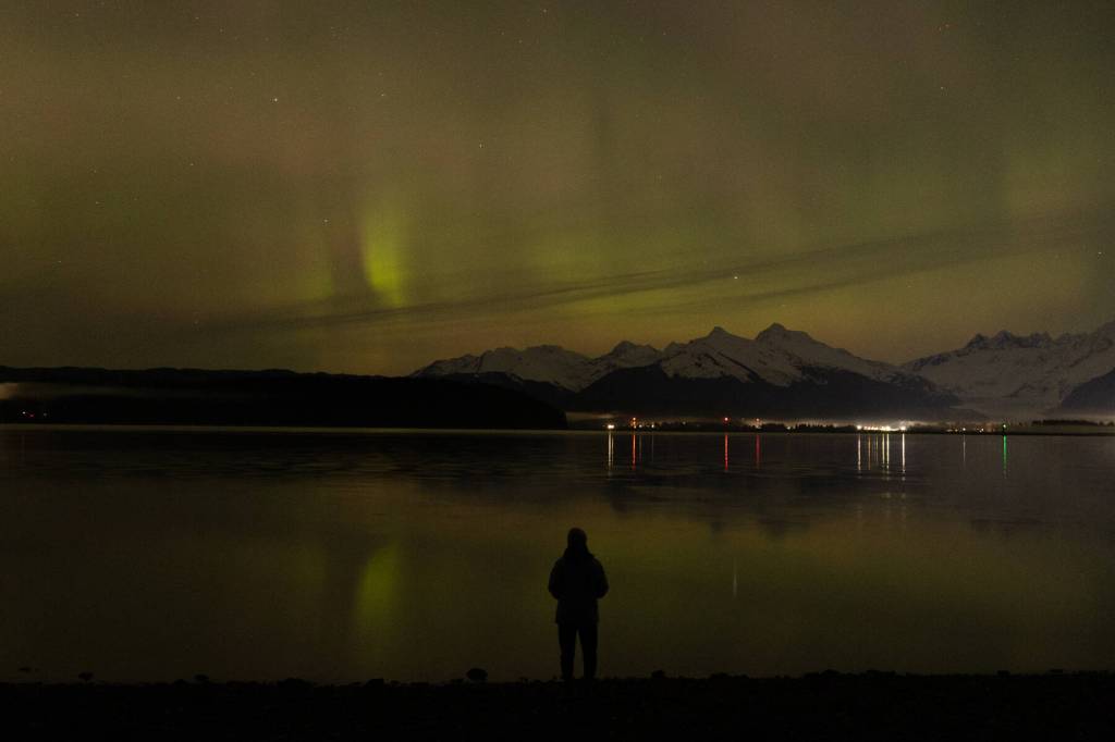 Juneau Empire reporter Mari Kanagy watches the northern lights dance over the Mendenhall Valley from the North Douglas launch ramp late Monday, Jan. 19. (Chloe Anderson/Juneau Empire)